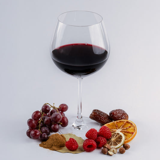 Glass of red wine with grapes, raspberries, and dried oranges on a light gray background